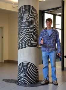 Student poses with artwork on a pillar.