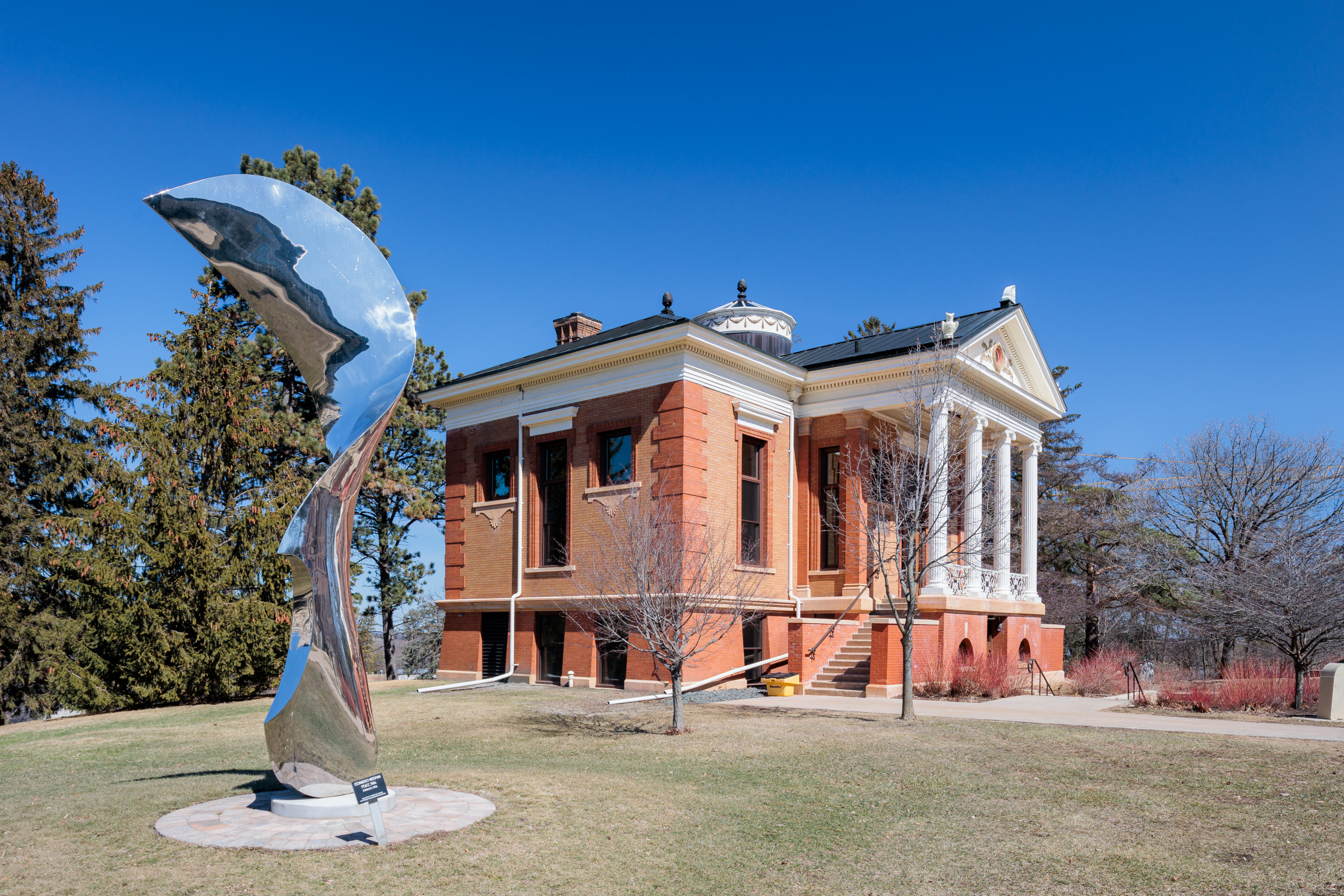 Side exterior of Steensland Hall. There is a sculpture to the left of Steensland Hall, and it is tall, silver, abstract, and modern.